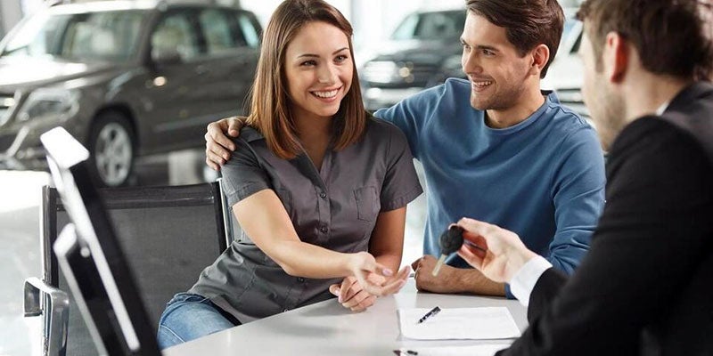 Smiling couple at dealership being handed vehicle keys